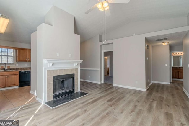 unfurnished living room with lofted ceiling, sink, a tiled fireplace, ceiling fan, and light hardwood / wood-style flooring