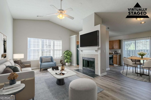 living room featuring a tiled fireplace, lofted ceiling, ceiling fan, and light hardwood / wood-style flooring