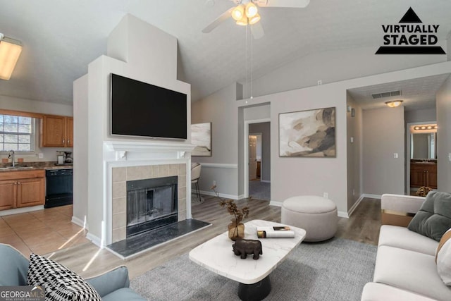 living room with lofted ceiling, sink, light wood-type flooring, ceiling fan, and a tiled fireplace