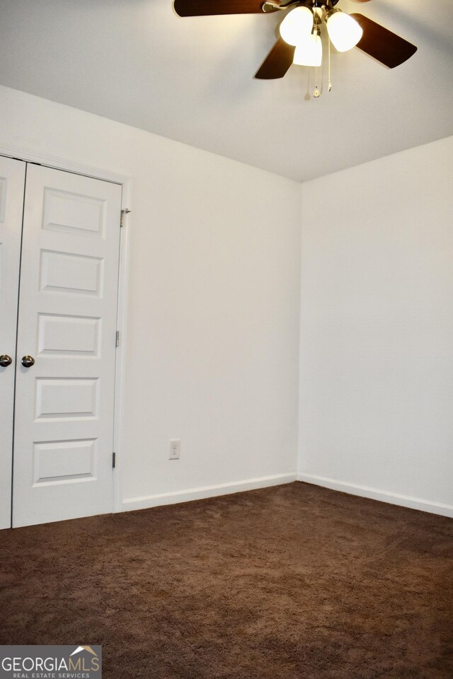 empty room featuring ceiling fan and dark colored carpet