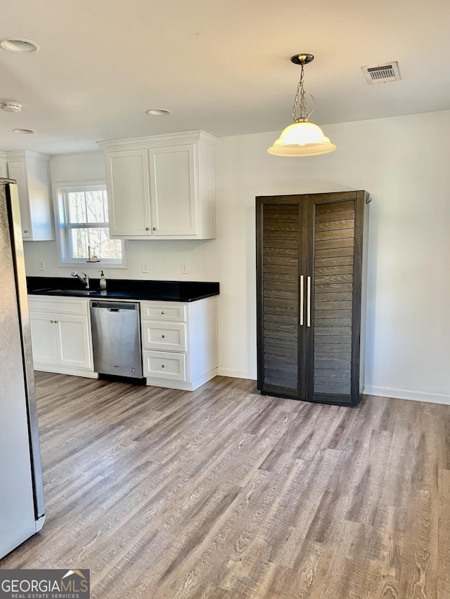 kitchen with appliances with stainless steel finishes, decorative light fixtures, white cabinetry, sink, and light hardwood / wood-style floors