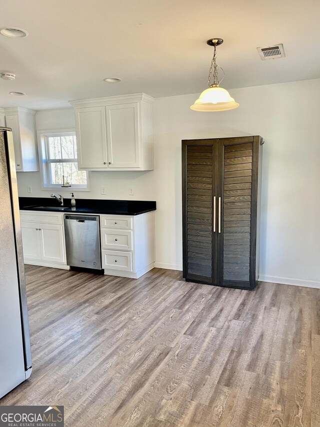 kitchen with appliances with stainless steel finishes, decorative light fixtures, white cabinetry, sink, and light hardwood / wood-style floors