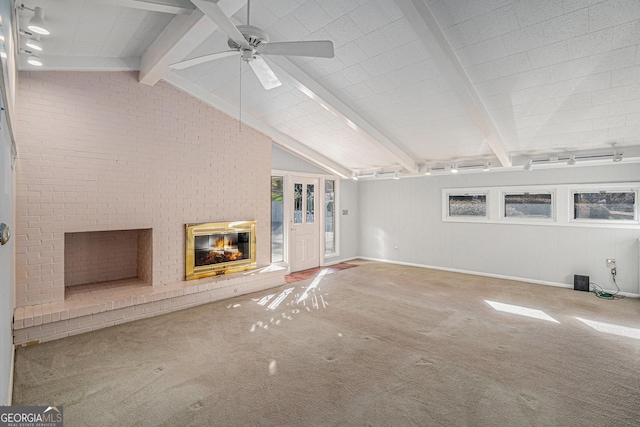 unfurnished living room with ceiling fan, carpet, a fireplace, lofted ceiling with beams, and brick wall