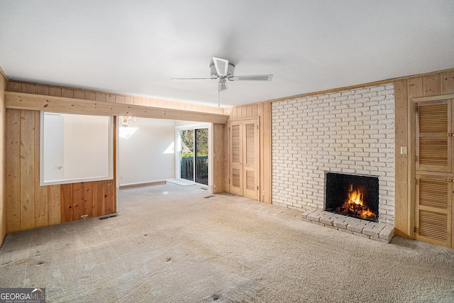 unfurnished living room with a brick fireplace, carpet floors, ceiling fan, and wood walls