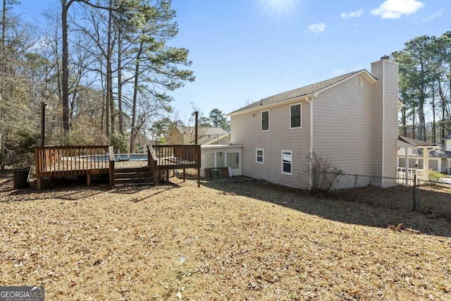 back of property with a deck, a chimney, and fence