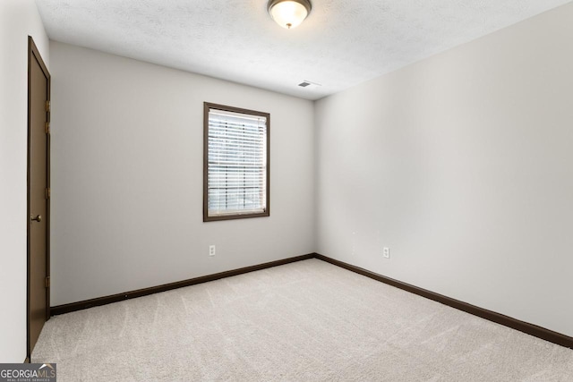 spare room featuring light carpet, a textured ceiling, and baseboards