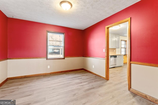 empty room featuring a textured ceiling, light wood finished floors, and baseboards