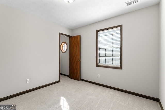 empty room featuring visible vents, light carpet, and baseboards