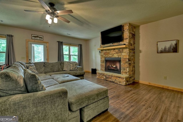 living room featuring ceiling fan, a healthy amount of sunlight, dark wood-type flooring, and a fireplace