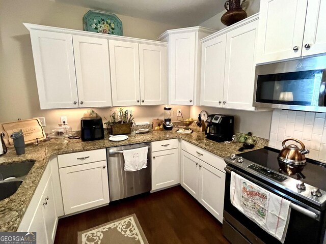 kitchen featuring appliances with stainless steel finishes, white cabinetry, sink, dark hardwood / wood-style flooring, and light stone countertops