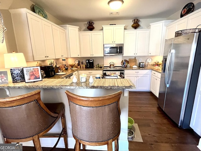 kitchen with appliances with stainless steel finishes, a breakfast bar, white cabinets, kitchen peninsula, and dark wood-type flooring