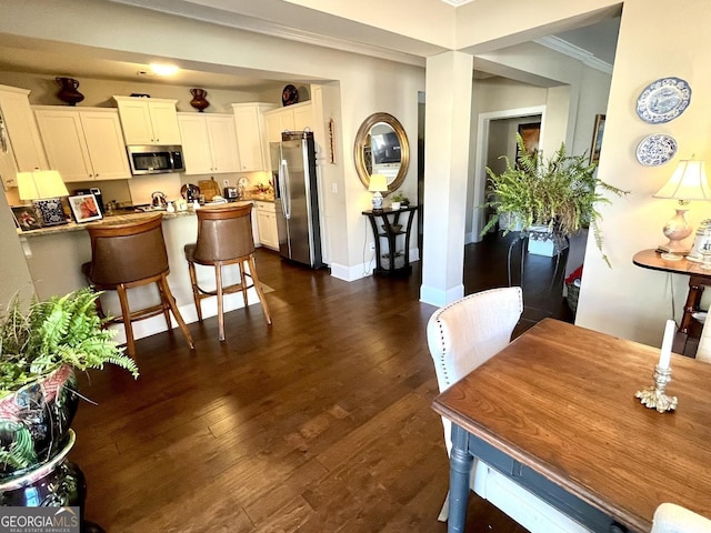 kitchen featuring a breakfast bar, crown molding, appliances with stainless steel finishes, dark hardwood / wood-style flooring, and white cabinets