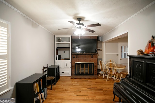 living room featuring ornamental molding, light wood-type flooring, ceiling fan, and a fireplace