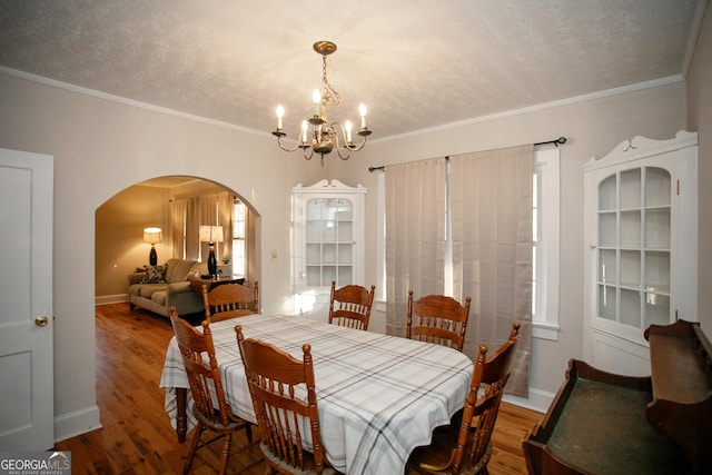 dining room with ornamental molding, wood-type flooring, a textured ceiling, and a notable chandelier