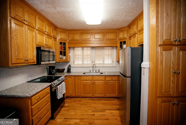 kitchen featuring sink, decorative backsplash, light stone counters, light hardwood / wood-style floors, and stainless steel appliances