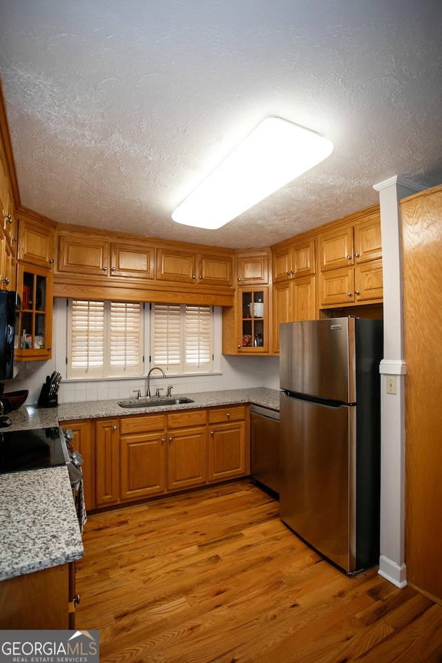 kitchen with sink, light stone counters, stainless steel appliances, a textured ceiling, and light hardwood / wood-style flooring