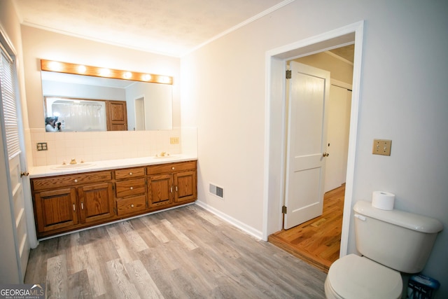 bathroom featuring toilet, tasteful backsplash, crown molding, wood-type flooring, and vanity