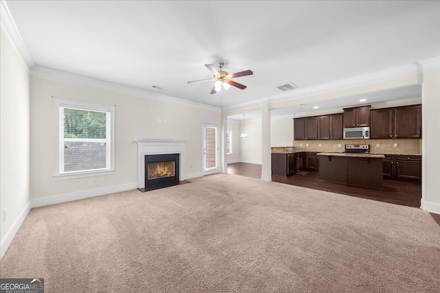 unfurnished living room with ceiling fan, ornamental molding, and carpet floors