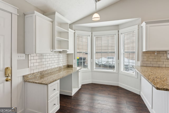 kitchen featuring lofted ceiling, built in desk, light stone countertops, white cabinets, and decorative light fixtures