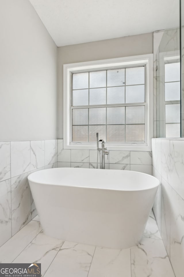 bathroom with plenty of natural light, a washtub, and tile walls