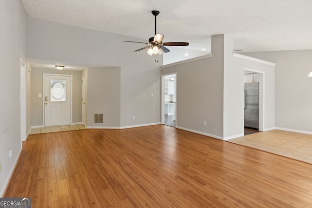 unfurnished living room with vaulted ceiling, a textured ceiling, ceiling fan, and light hardwood / wood-style flooring