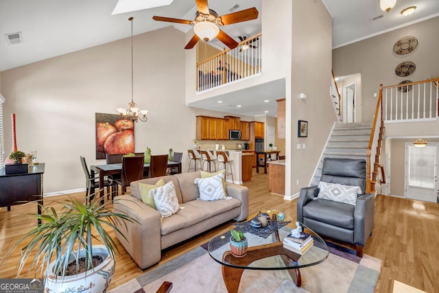 living area featuring baseboards, visible vents, light wood-style flooring, stairs, and high vaulted ceiling