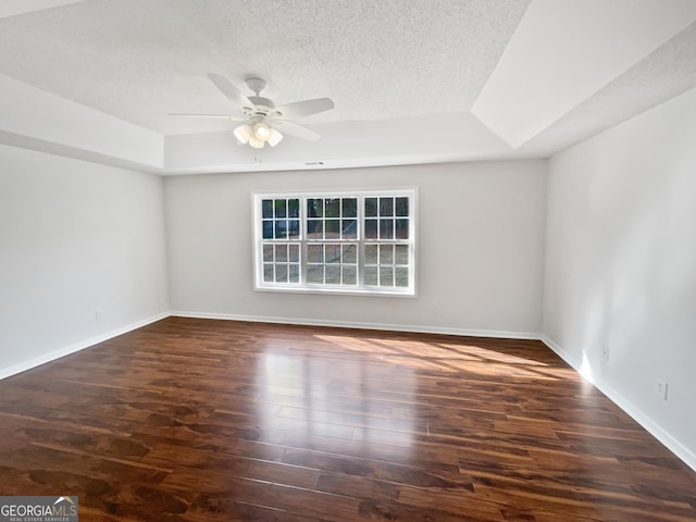 empty room featuring dark wood-type flooring, ceiling fan, a raised ceiling, and a textured ceiling