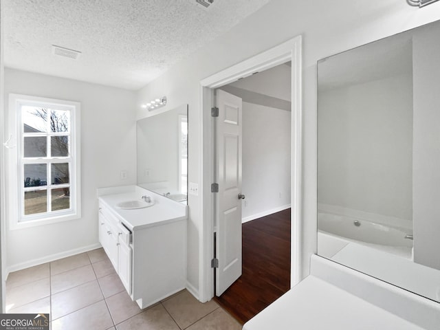 bathroom featuring tile patterned flooring, vanity, a bath, and a textured ceiling