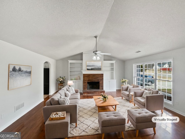 living room featuring vaulted ceiling, a textured ceiling, built in features, hardwood / wood-style flooring, and a fireplace