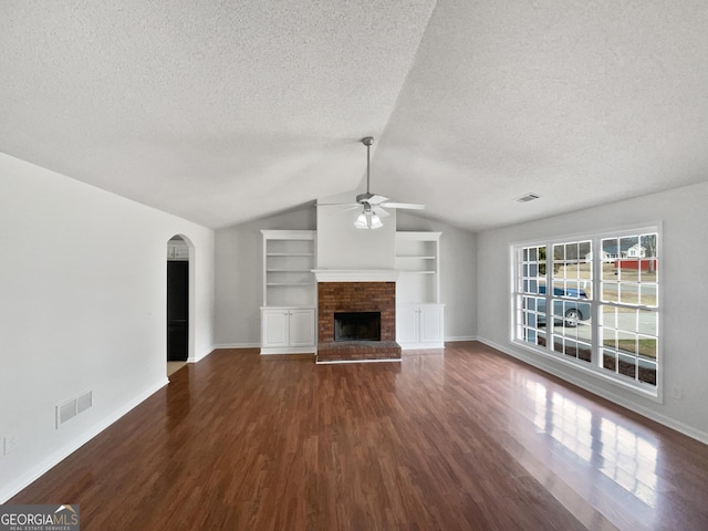 unfurnished living room with dark wood-type flooring, ceiling fan, a fireplace, a textured ceiling, and built in shelves