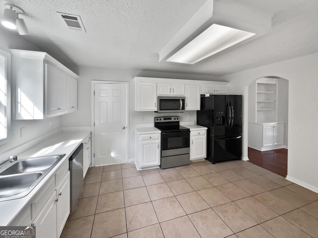 kitchen featuring sink, a textured ceiling, light tile patterned floors, stainless steel appliances, and white cabinets