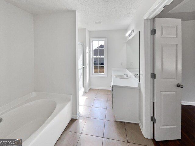 bathroom featuring tile patterned flooring, vanity, a washtub, and a textured ceiling