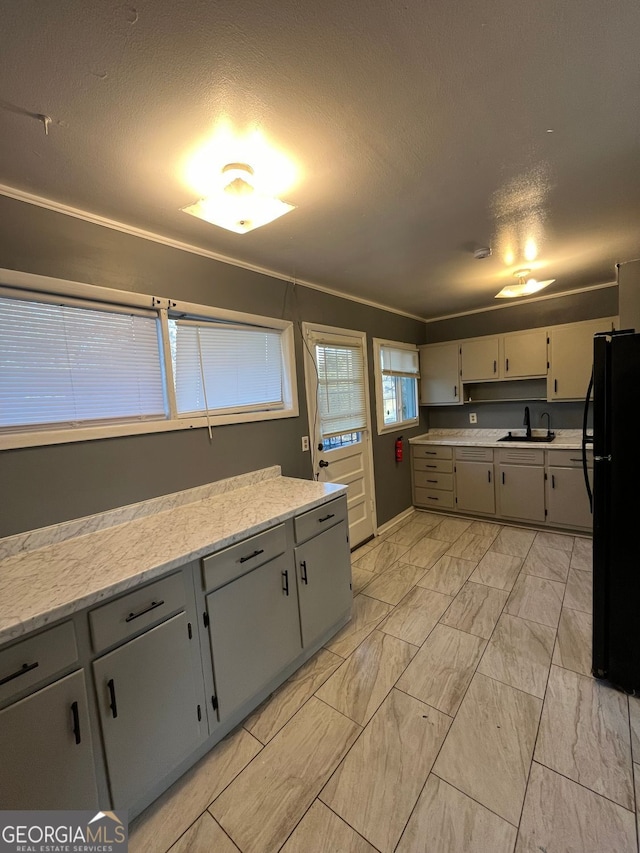 kitchen featuring sink, light stone countertops, a textured ceiling, and black fridge