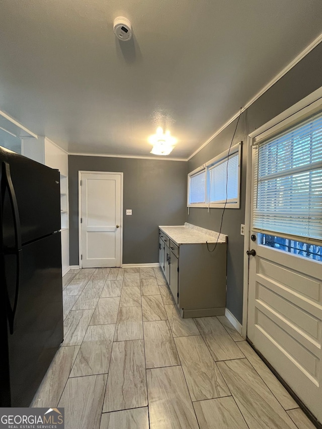 kitchen featuring black refrigerator, light stone counters, gray cabinets, and ornamental molding