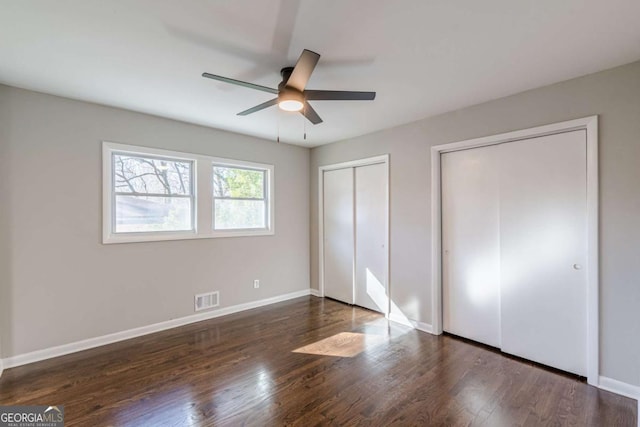 unfurnished bedroom featuring ceiling fan, dark hardwood / wood-style flooring, and two closets