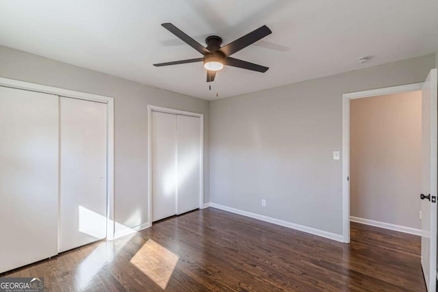 unfurnished bedroom with ceiling fan, dark hardwood / wood-style floors, and two closets