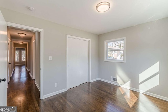 unfurnished bedroom featuring a closet, dark hardwood / wood-style flooring, and multiple windows