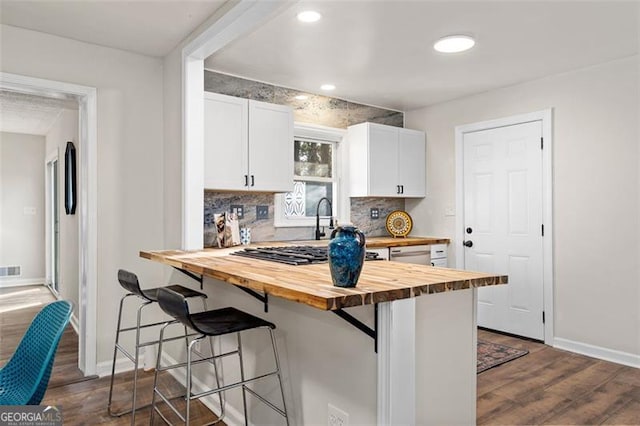 kitchen with white cabinetry, backsplash, dark hardwood / wood-style flooring, wooden counters, and a kitchen bar