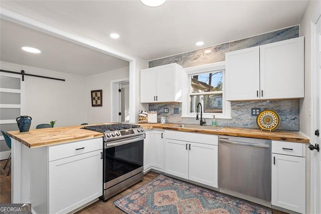 kitchen with sink, butcher block counters, stainless steel appliances, white cabinets, and a barn door