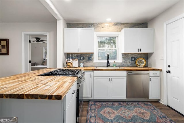 kitchen featuring stainless steel dishwasher, wooden counters, sink, and white cabinets