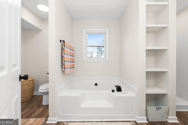 bathroom with hardwood / wood-style flooring, built in features, a bathtub, and toilet