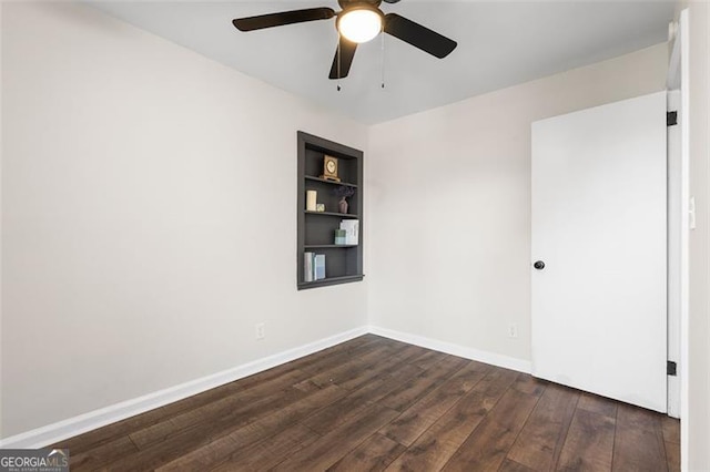 empty room featuring dark hardwood / wood-style flooring, built in shelves, and ceiling fan