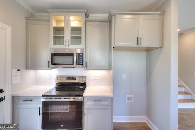 kitchen featuring dark hardwood / wood-style flooring, backsplash, crown molding, and appliances with stainless steel finishes