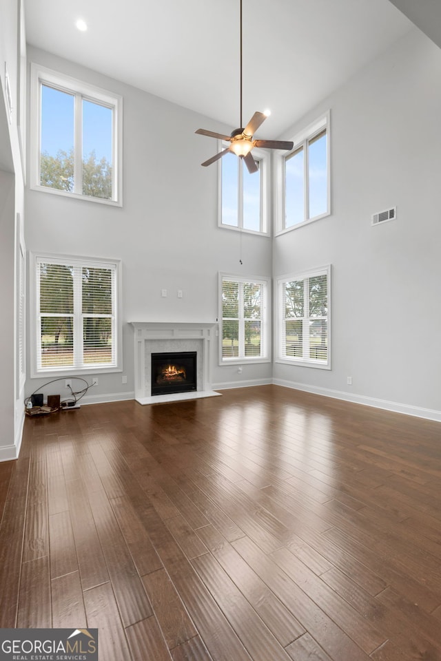 unfurnished living room featuring hardwood / wood-style flooring, a high end fireplace, ceiling fan, and a towering ceiling