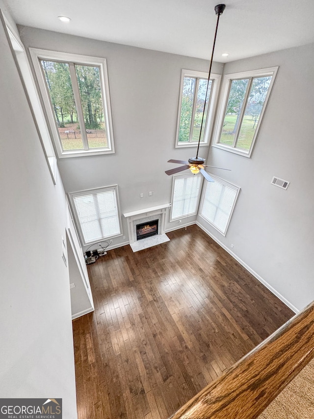 unfurnished living room with dark wood-type flooring, ceiling fan, a premium fireplace, and a wealth of natural light