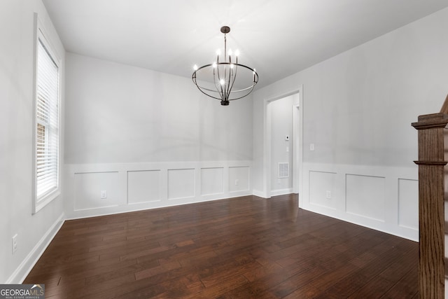 unfurnished dining area with dark wood-type flooring and an inviting chandelier