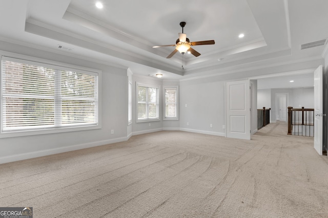 empty room with ceiling fan, light colored carpet, ornamental molding, and a raised ceiling