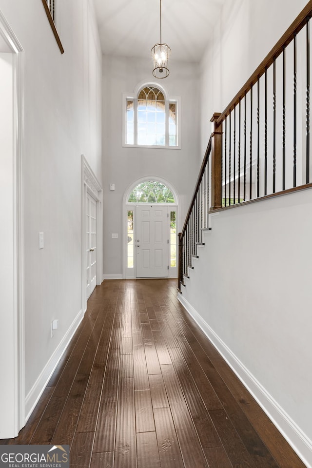 entryway featuring a notable chandelier, a towering ceiling, and dark wood-type flooring