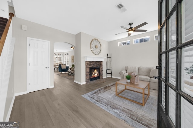 living room featuring wood-type flooring, a stone fireplace, and ceiling fan