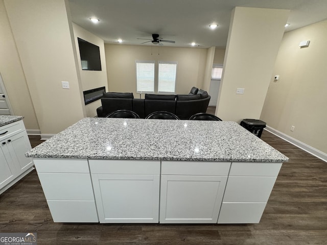 kitchen with a breakfast bar, white cabinetry, light stone counters, a kitchen island, and dark hardwood / wood-style flooring